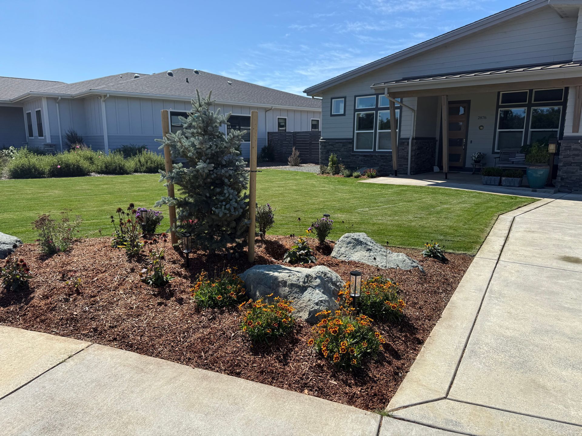 Green lawn borders a lush garden with diverse plants and trees.