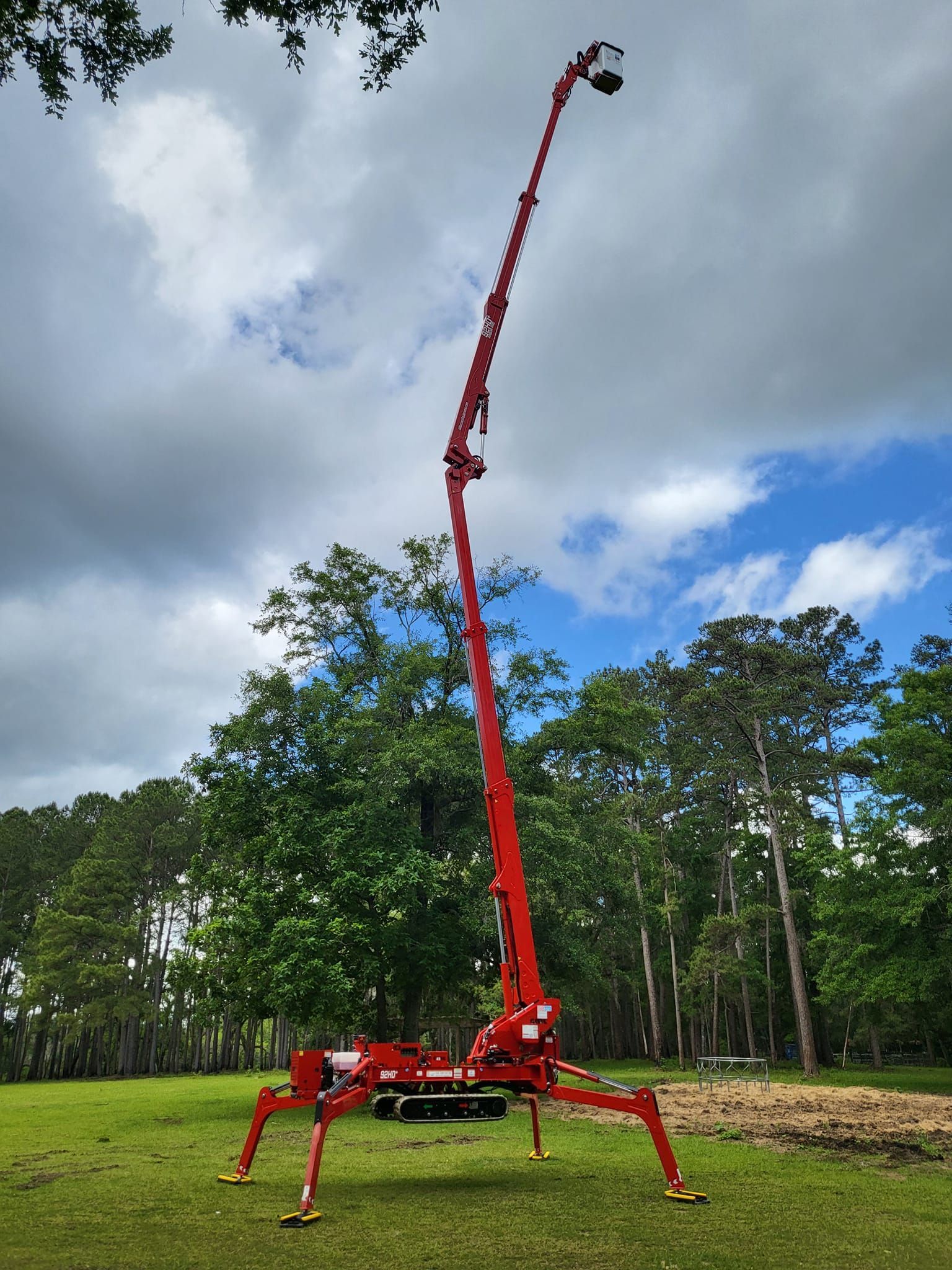 Red spider crane with a long boom raised high in a grassy field under cloudy sky