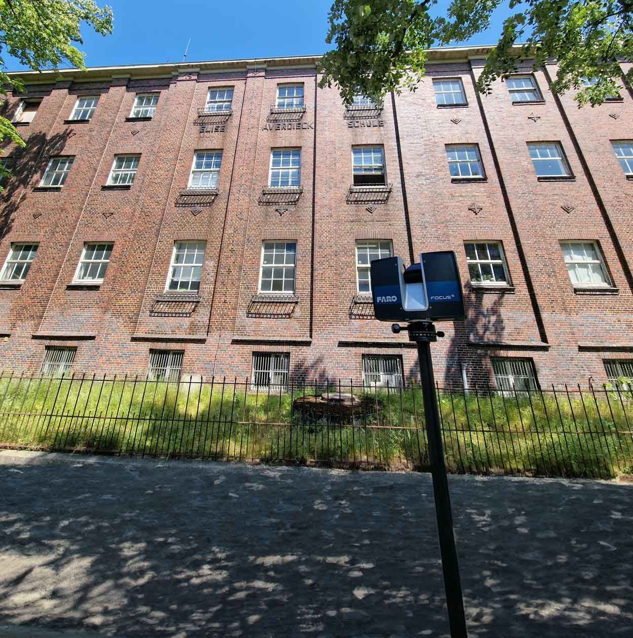 Fassade eines Gebäudes mit vielen Fenstern vor dem der 3D- Lasescanner steht | THYEN Digitale Aufmaße