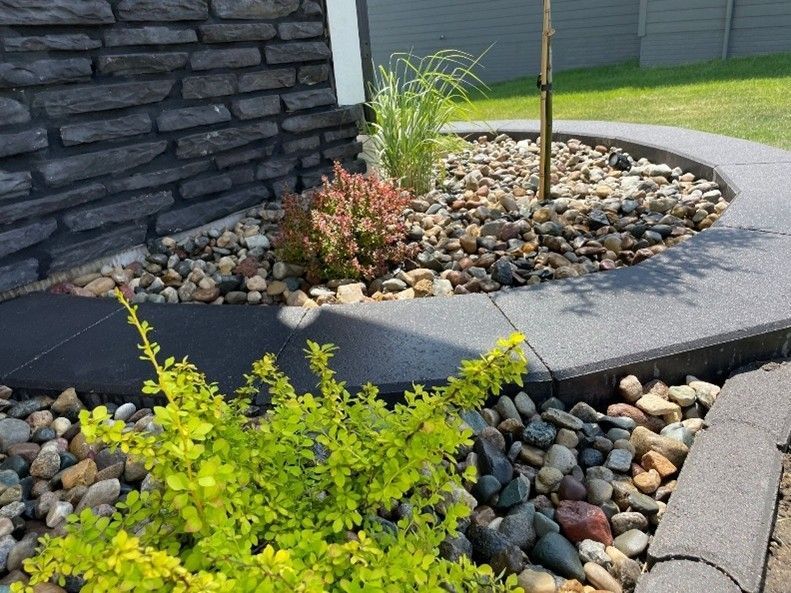 A modern landscaping with stone edging, decorative rocks, and small shrubs near a house wall