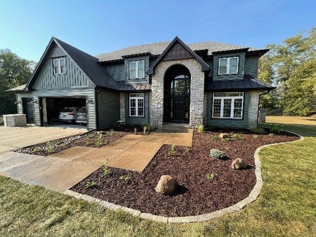 A front yard of a modern two-story house with fresh landscaping, mulch beds, and stone edging