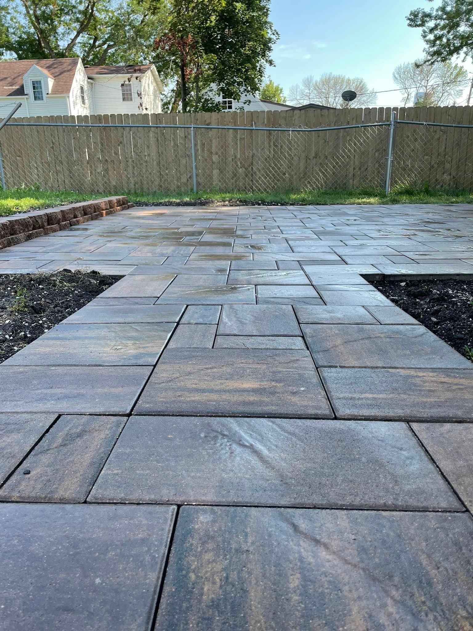 A patio with a fence in the background and a house in the background.