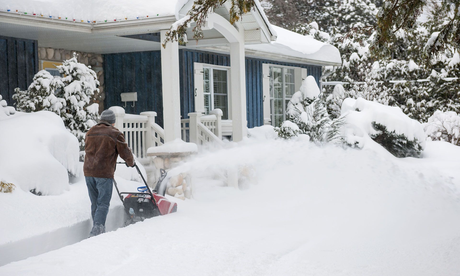 A man is pushing a snow blower in front of a house.