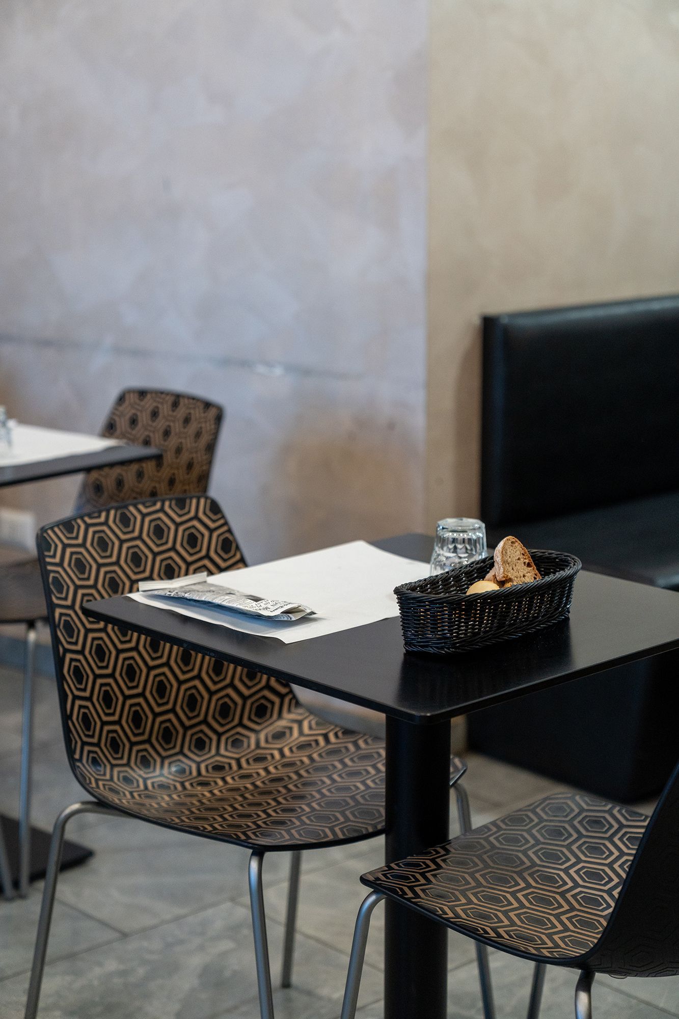 Interno del ristorante con tavoli neri, sedie a fantasia e un cestino del pane.