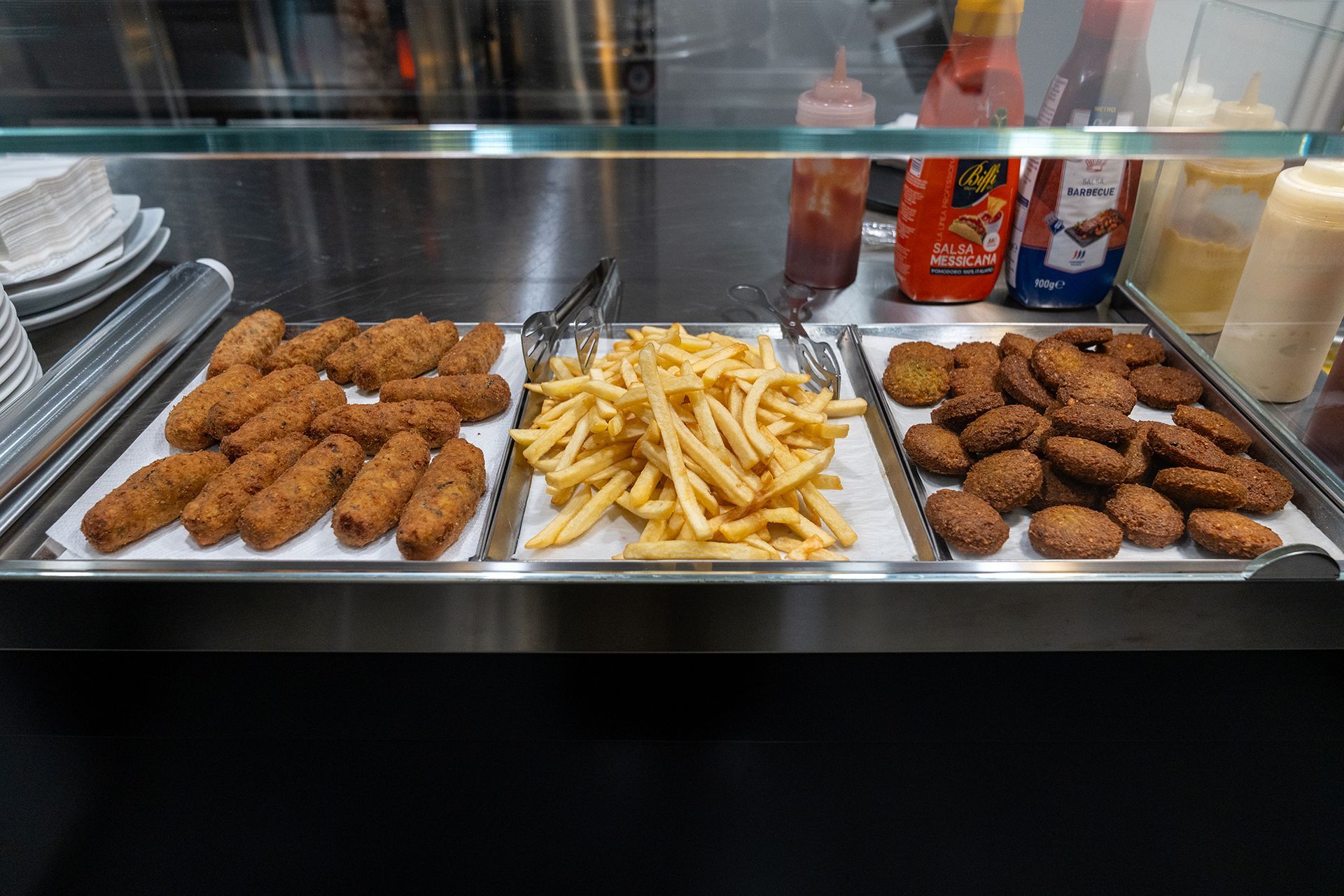 Vetrina con cibi fritti: bocconcini di pollo, patatine fritte e hamburger. Ketchup e salse a vista.