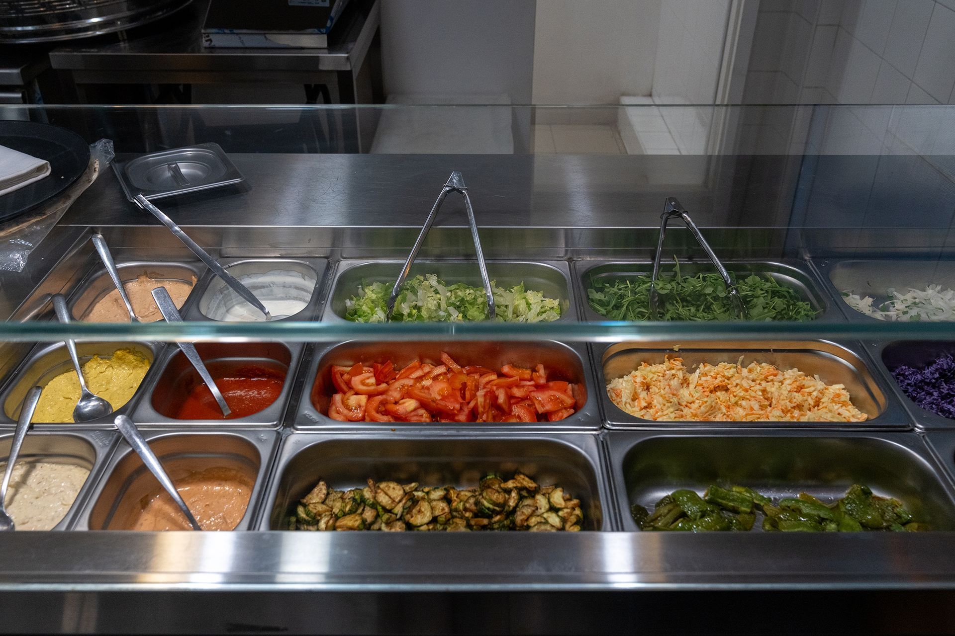 Esposizione di condimenti in un buffet in acciaio inossidabile, tra cui salse, verdure e kimchi.