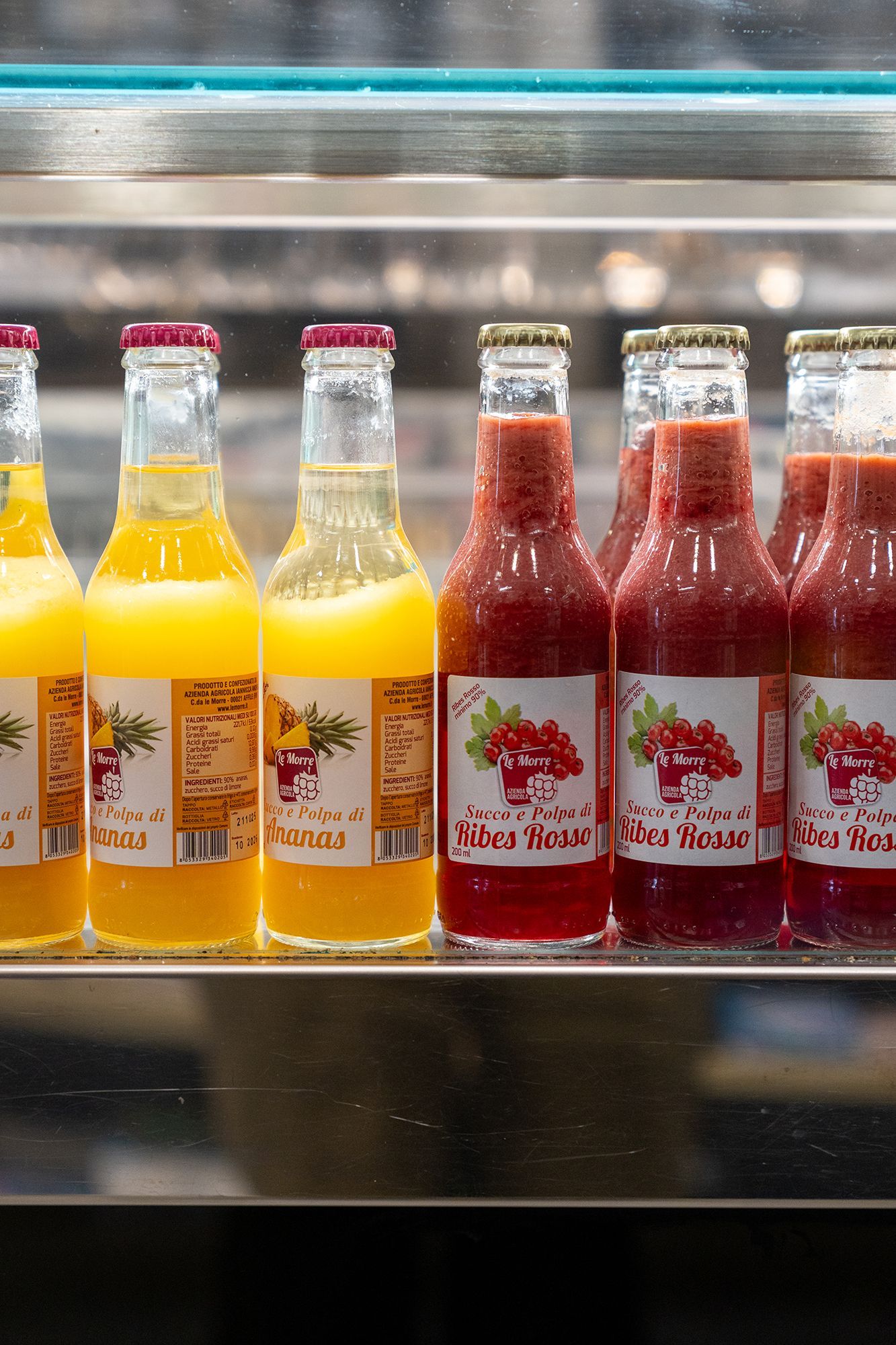 Bottiglie di succo, gialle e rosse, in una vetrina refrigerata.