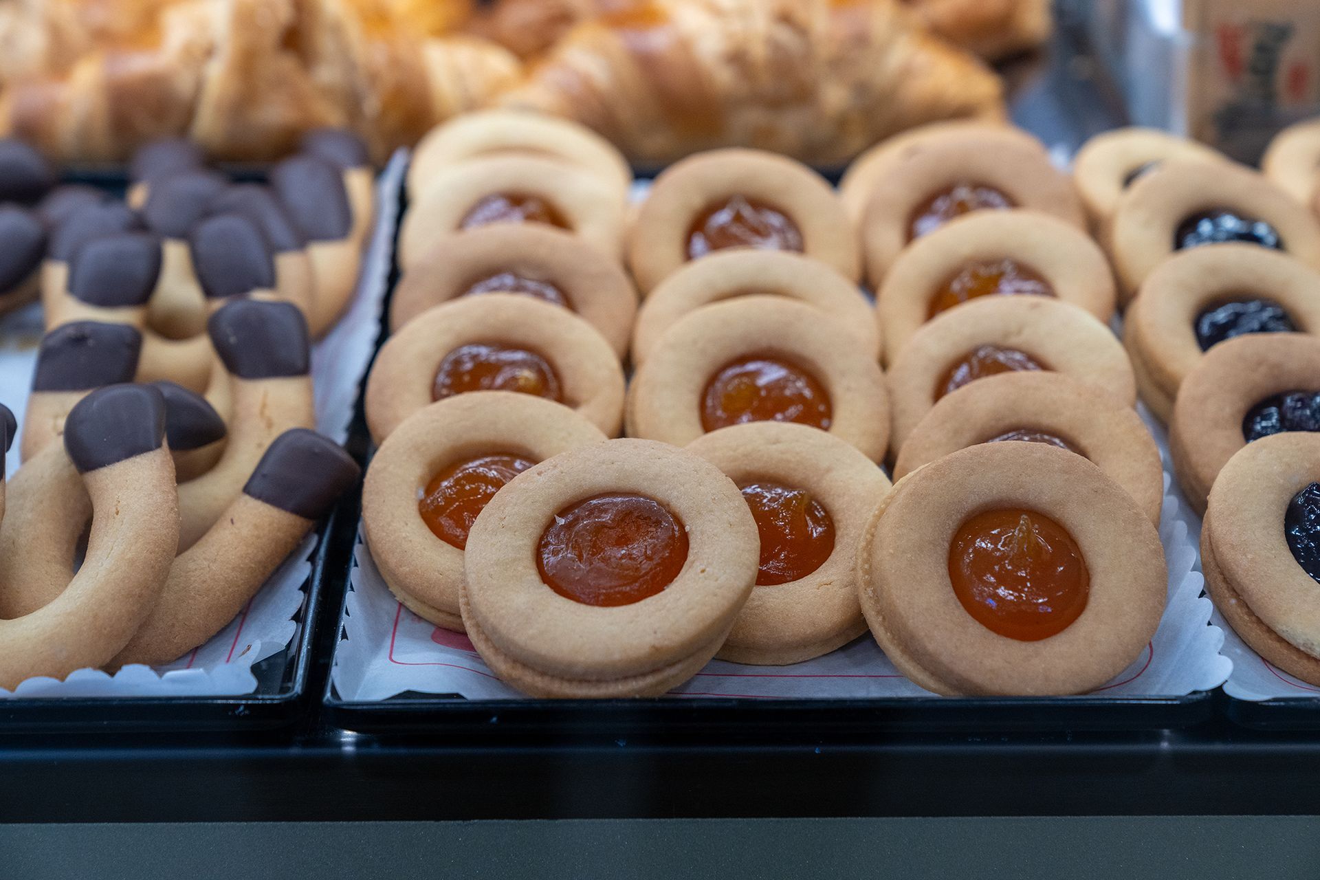 Esposizione di biscotti e pasticcini, con varietà ripiene di marmellata e ricoperte di cioccolato.