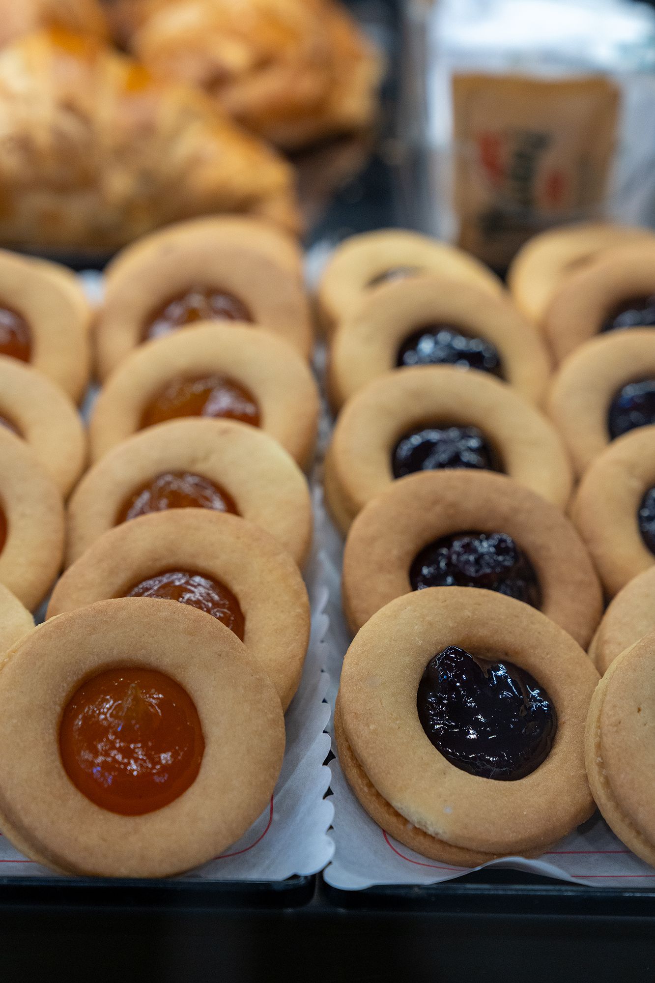Biscotti ripieni di marmellata esposti in una pasticceria. File di biscotti rotondi con ripieno arancione e viola.
