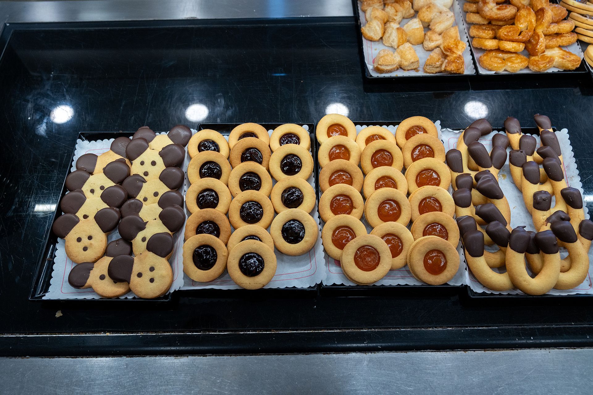 Biscotti disposti su un vassoio, con varietà ricoperte di cioccolato, ripiene di marmellata e a forma di anello.