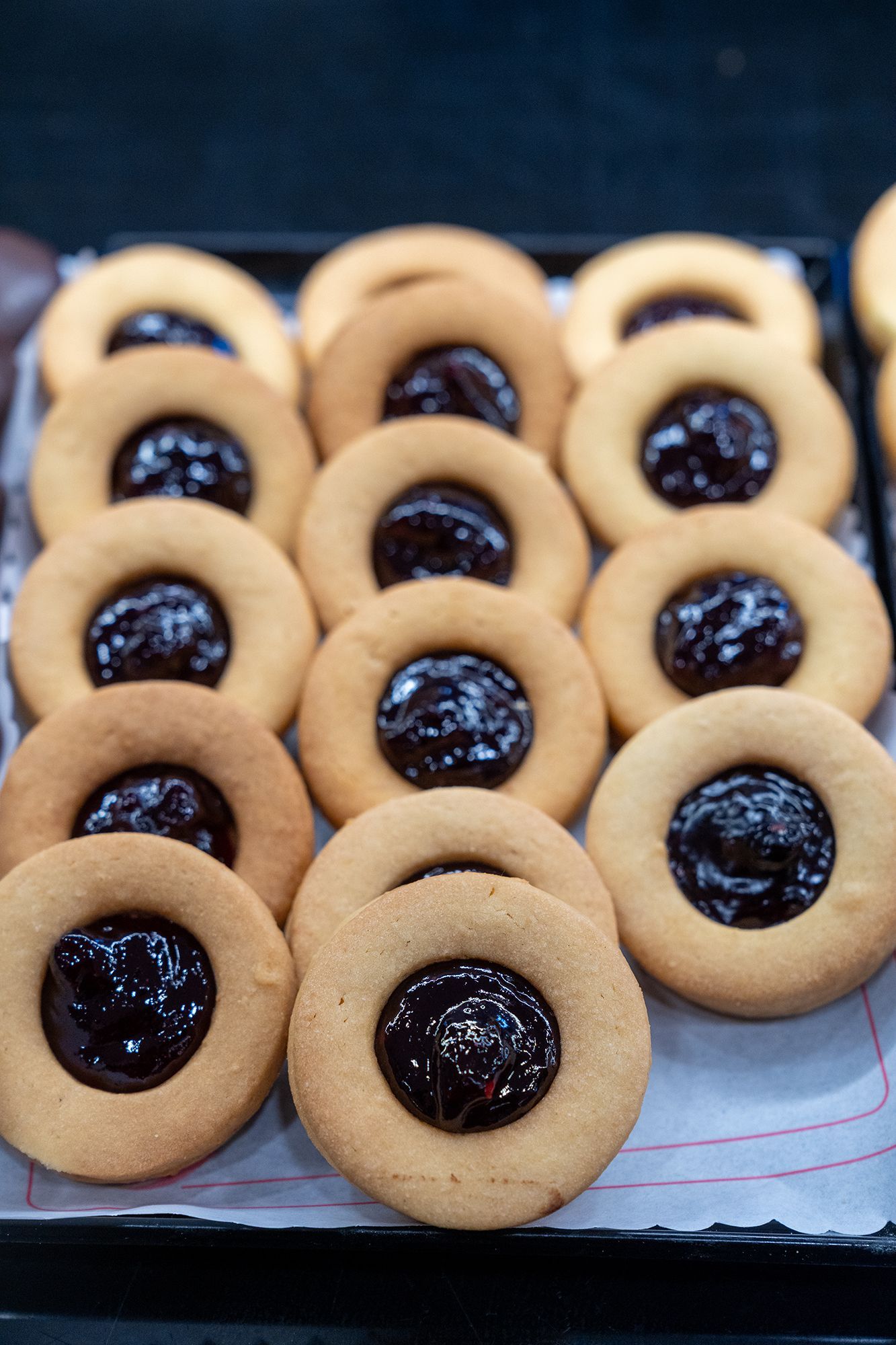 Biscotti con ripieno di marmellata scura, disposti su un vassoio.