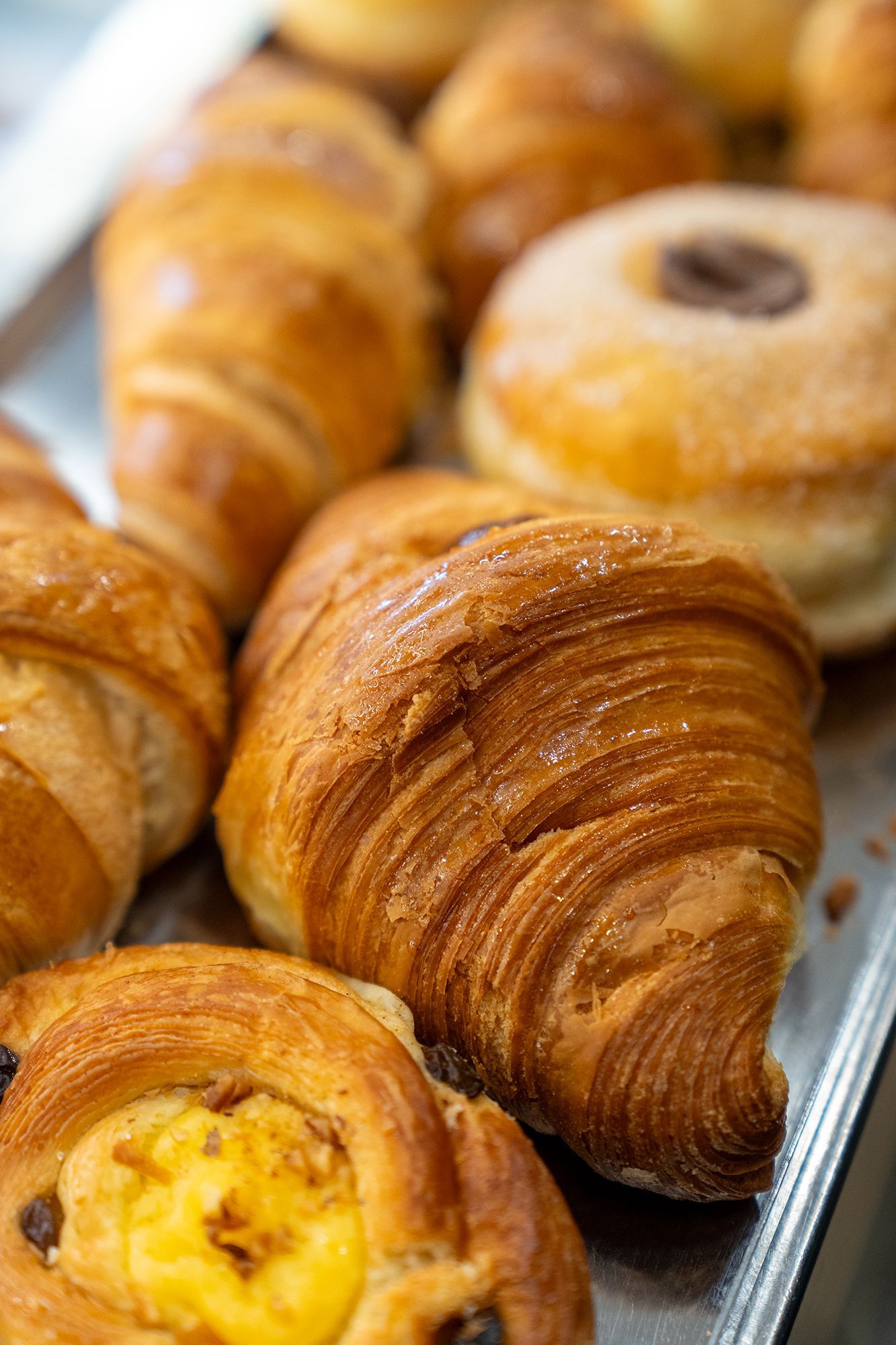 Primo piano di pasticcini, tra cui croissant e una ciambella, su un vassoio di metallo.