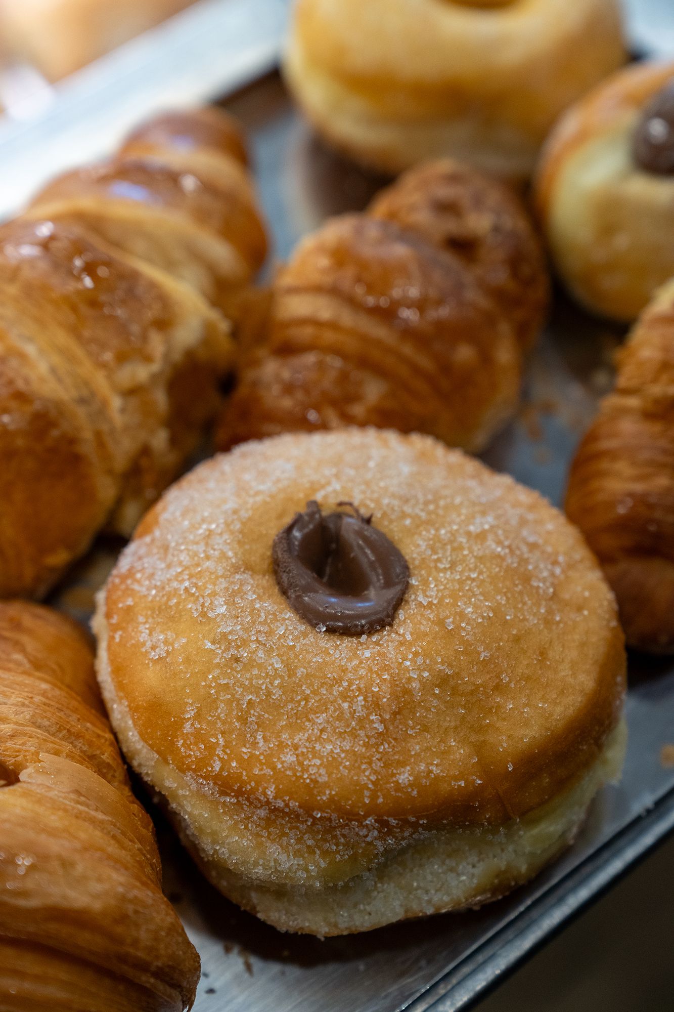Primo piano di dolci su un vassoio: croissant e ciambella ricoperta di zucchero e ripiena di cioccolato.