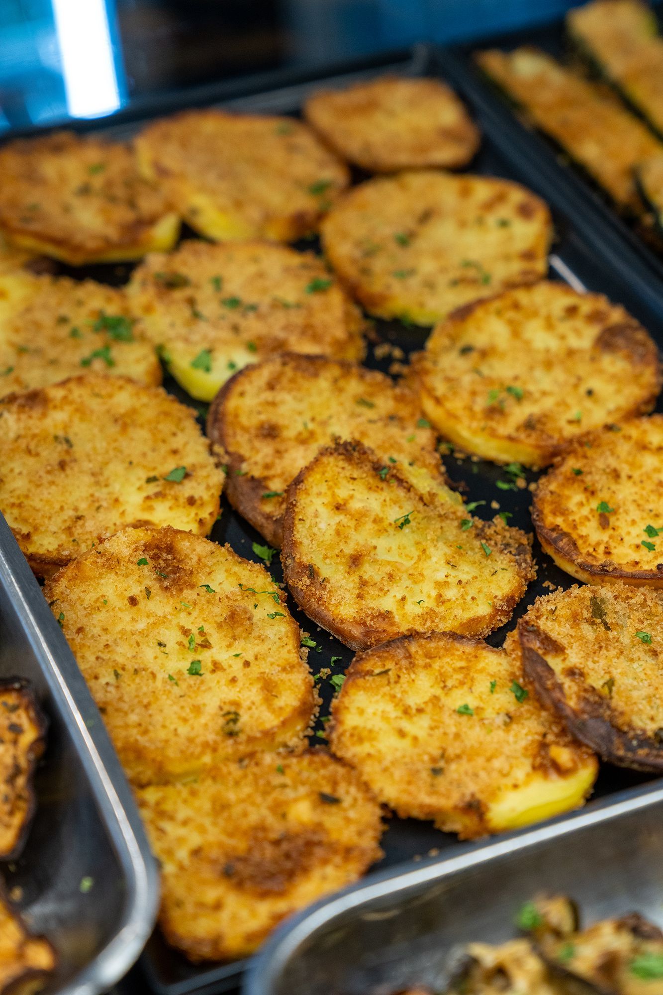 Vassoio di patate dorate, impanate, possibilmente cotte al forno o fritte, con erbe aromatiche, su un vassoio nero.