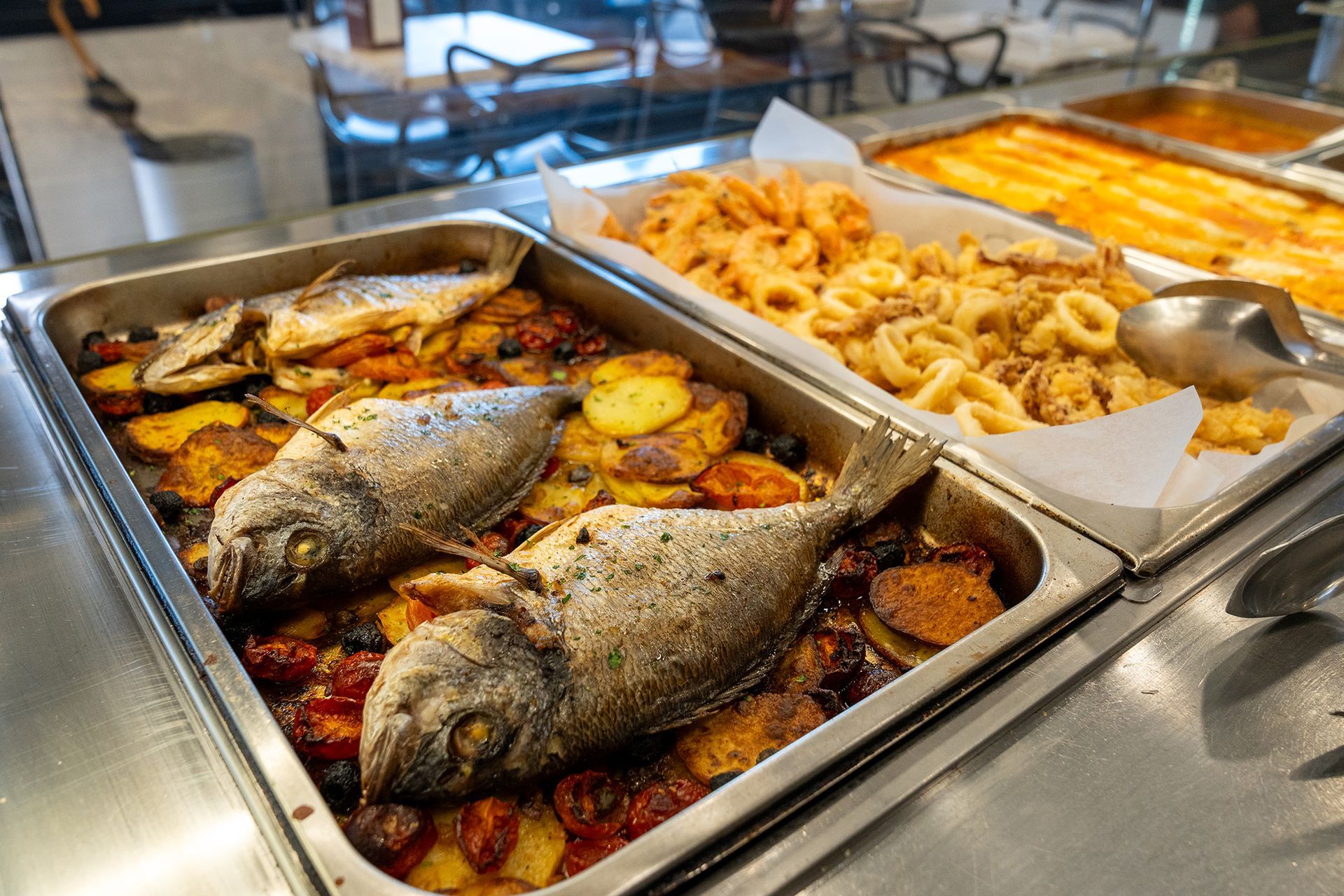 Pesce al forno con patate e pomodori, più calamari fritti, serviti a buffet.