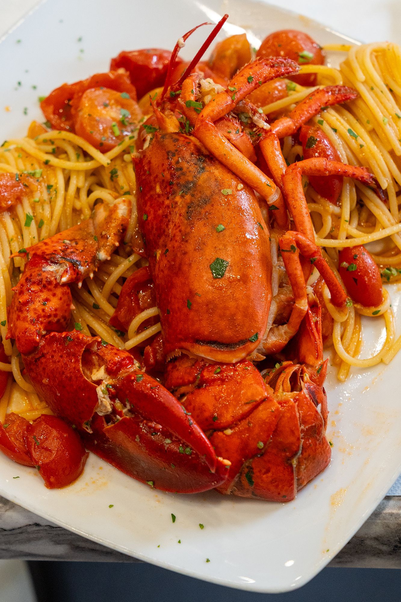 Piatto di aragosta e spaghetti con pomodorini su un piatto bianco.