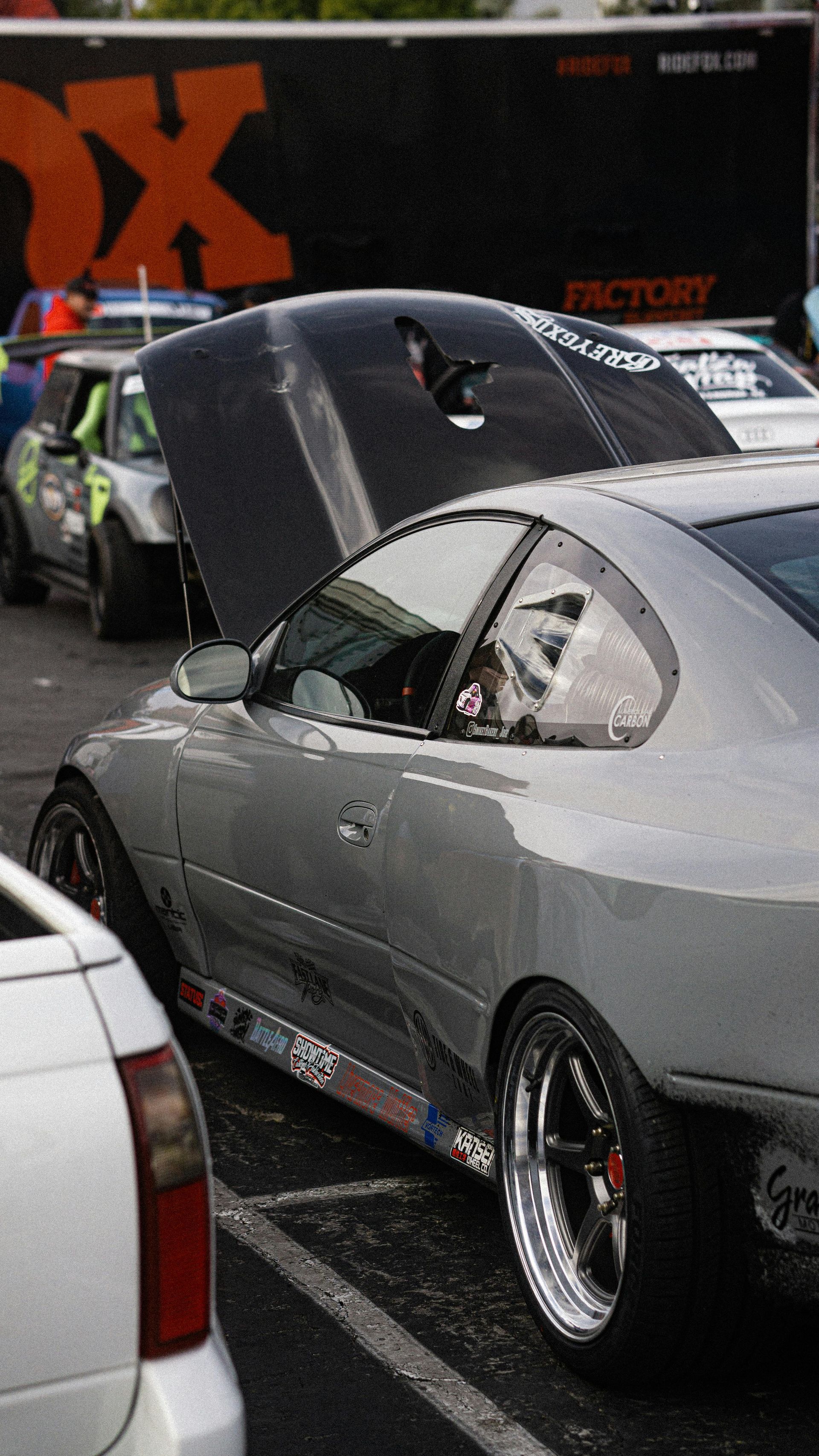 A silver car with the hood up is parked in a parking lot