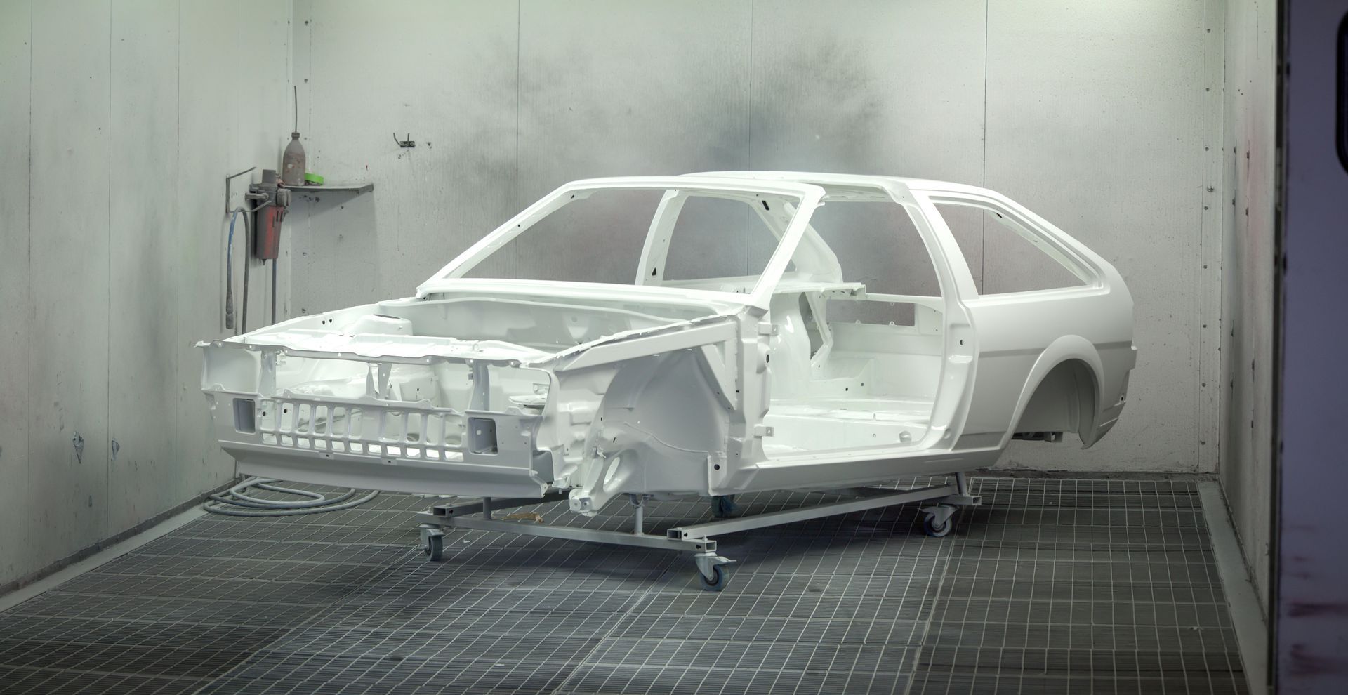 A white car is being painted in a paint booth