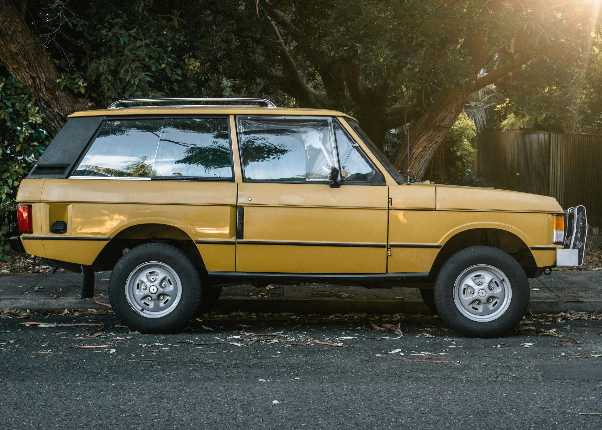 A yellow range rover is parked on the side of the road.