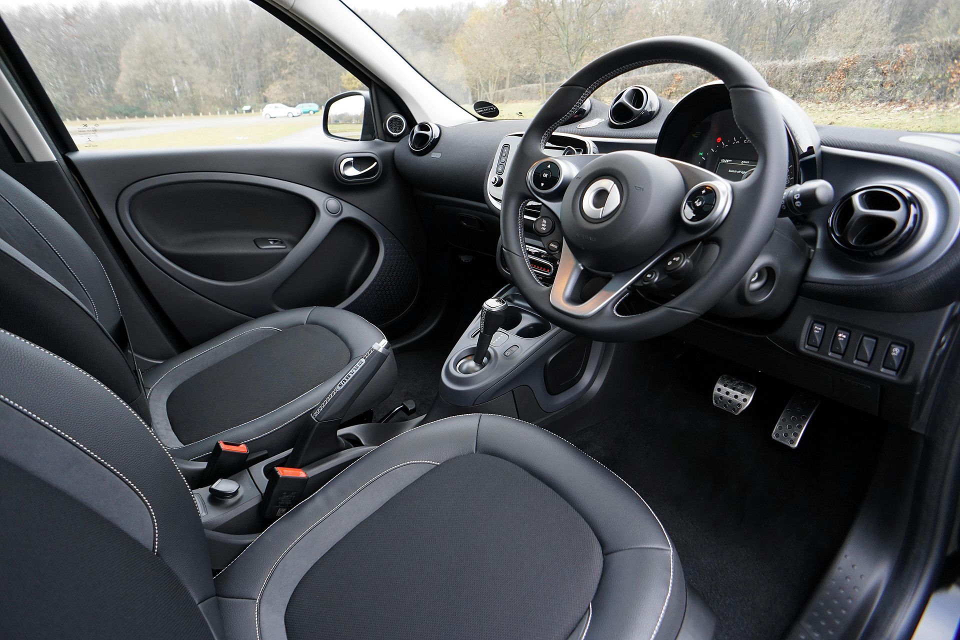 The interior of a smart car with black seats and a steering wheel.