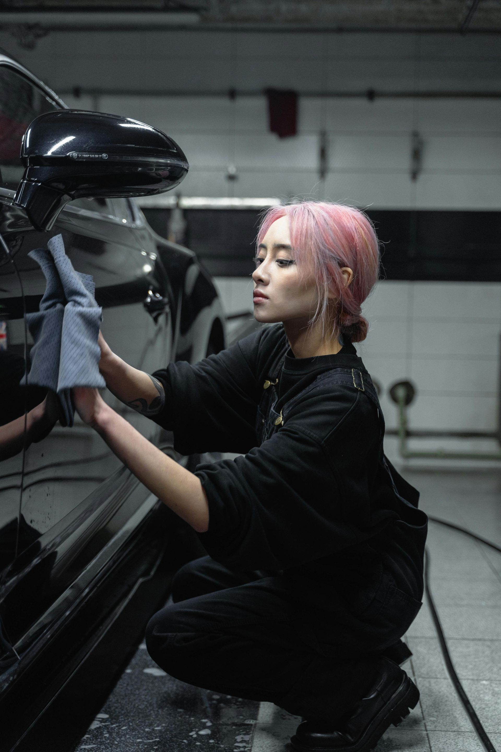 A woman is cleaning a car with a cloth in a garage.