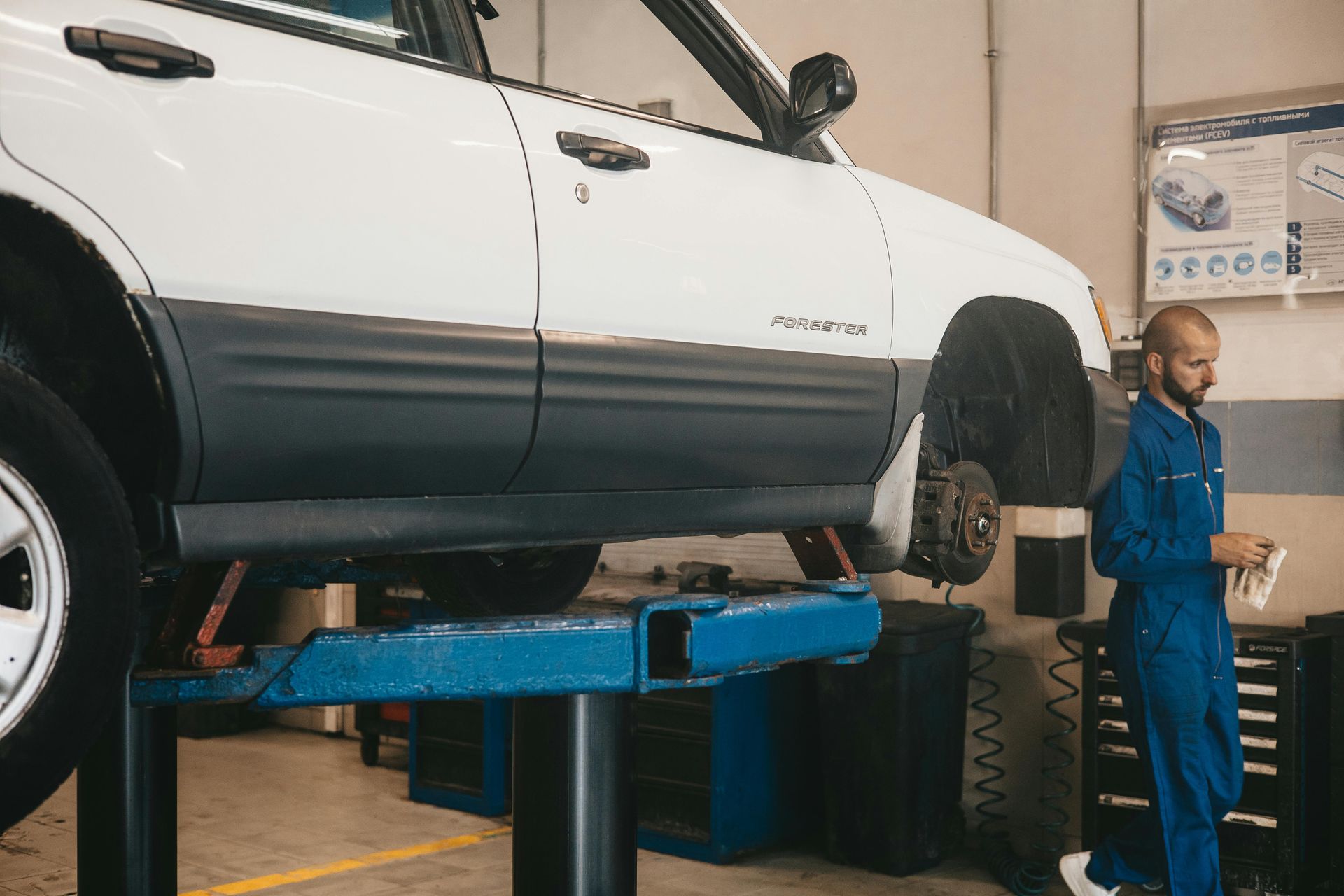 A man is standing next to a white car on a lift in a garage.