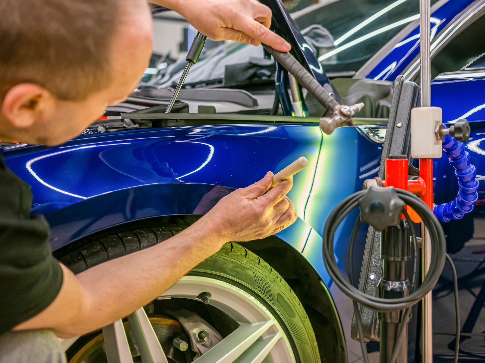 A man is working on a blue car with a hammer.