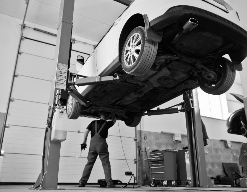 Mechanic working under a car lifted on a hydraulic hoist in a garage. | Reliable Automotive Repair