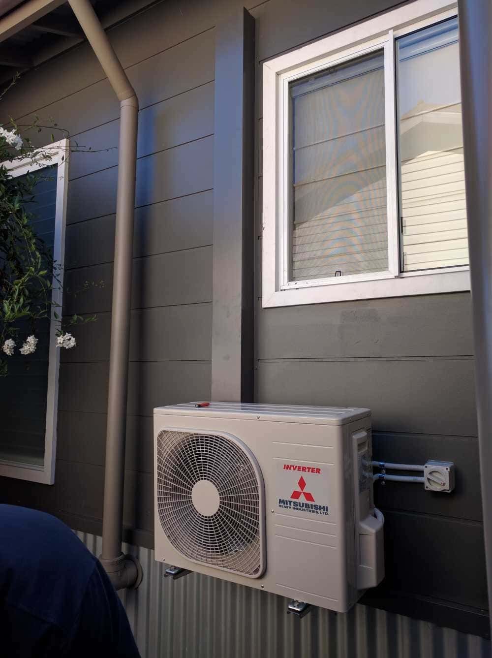 A Fan is Mounted on the Side of a Building Next to a Window — Cool Heat Air Conditioning in Albion Park, NSW