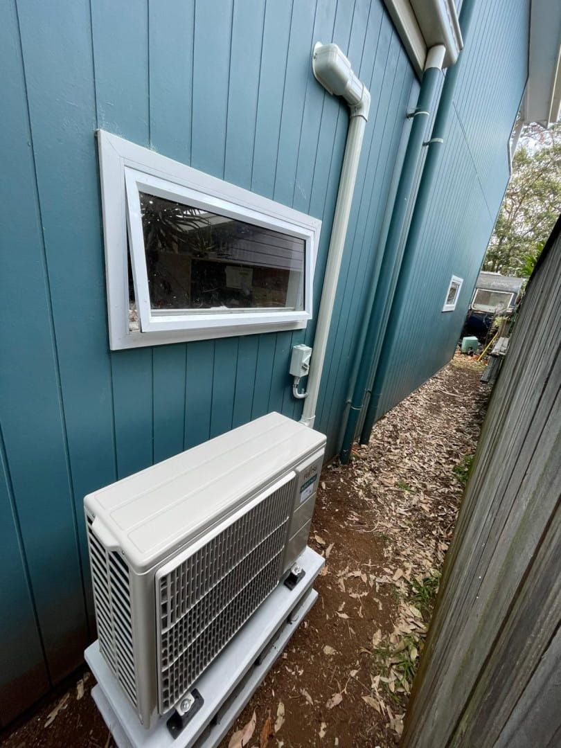 A White Air Conditioner on the Side of a Blue House Next to a Window — Cool Heat Air Conditioning in Albion Park, NSW