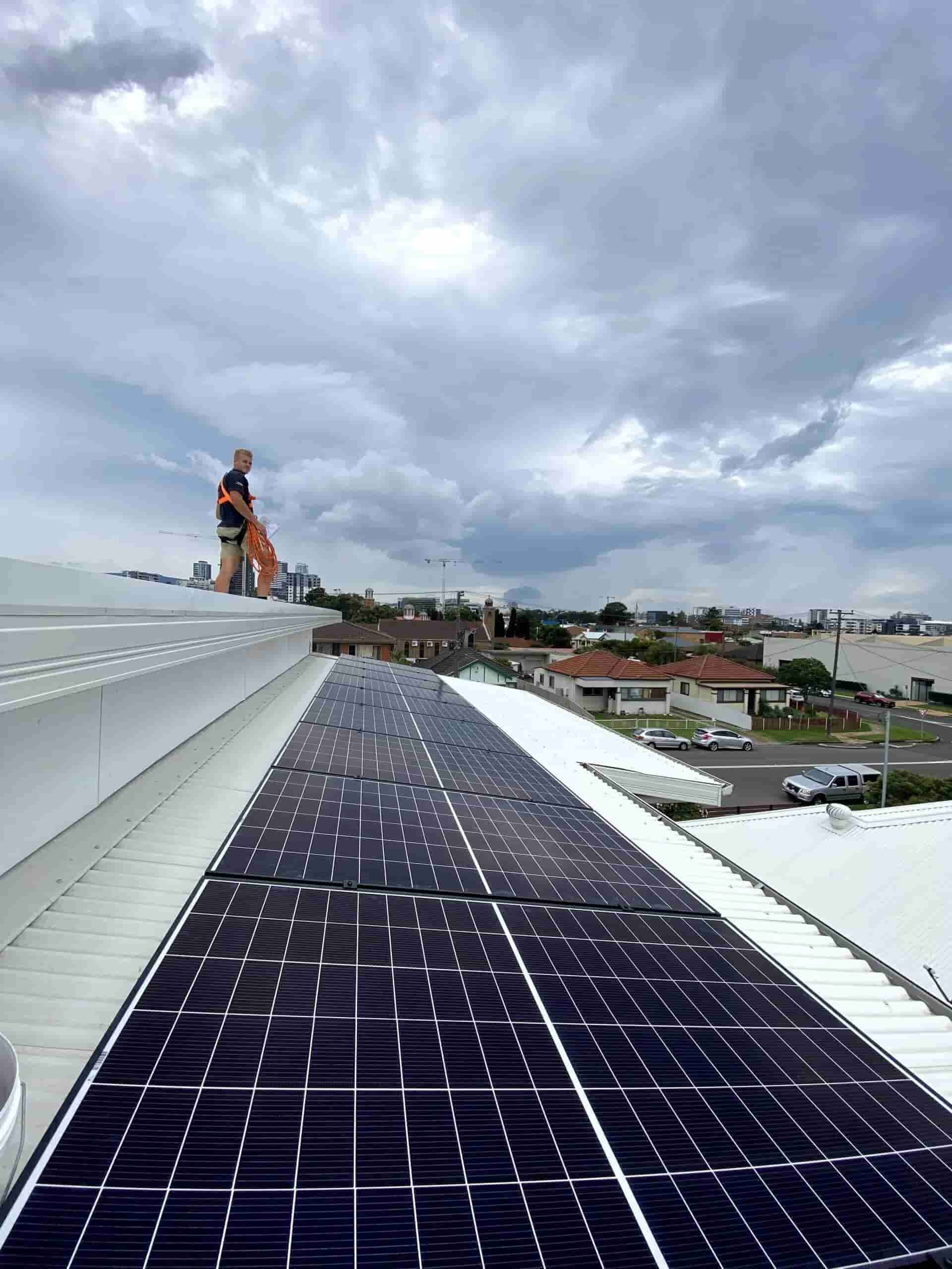 A Man is Standing on Top of a Roof With Solar Panels — Cool Heat Air Conditioning in Shellharbour, NSW