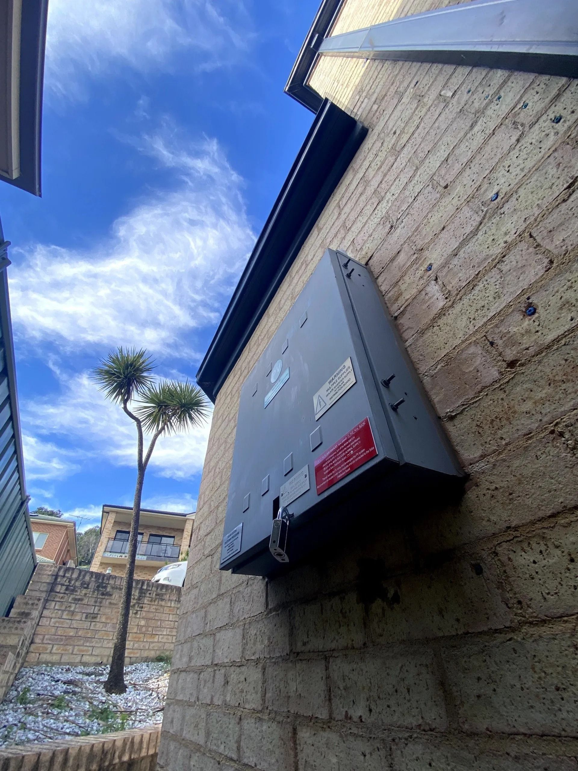 A Box on the Side of a Brick Building With a Tree — Cool Heat Air Conditioning in Albion Park, NSW