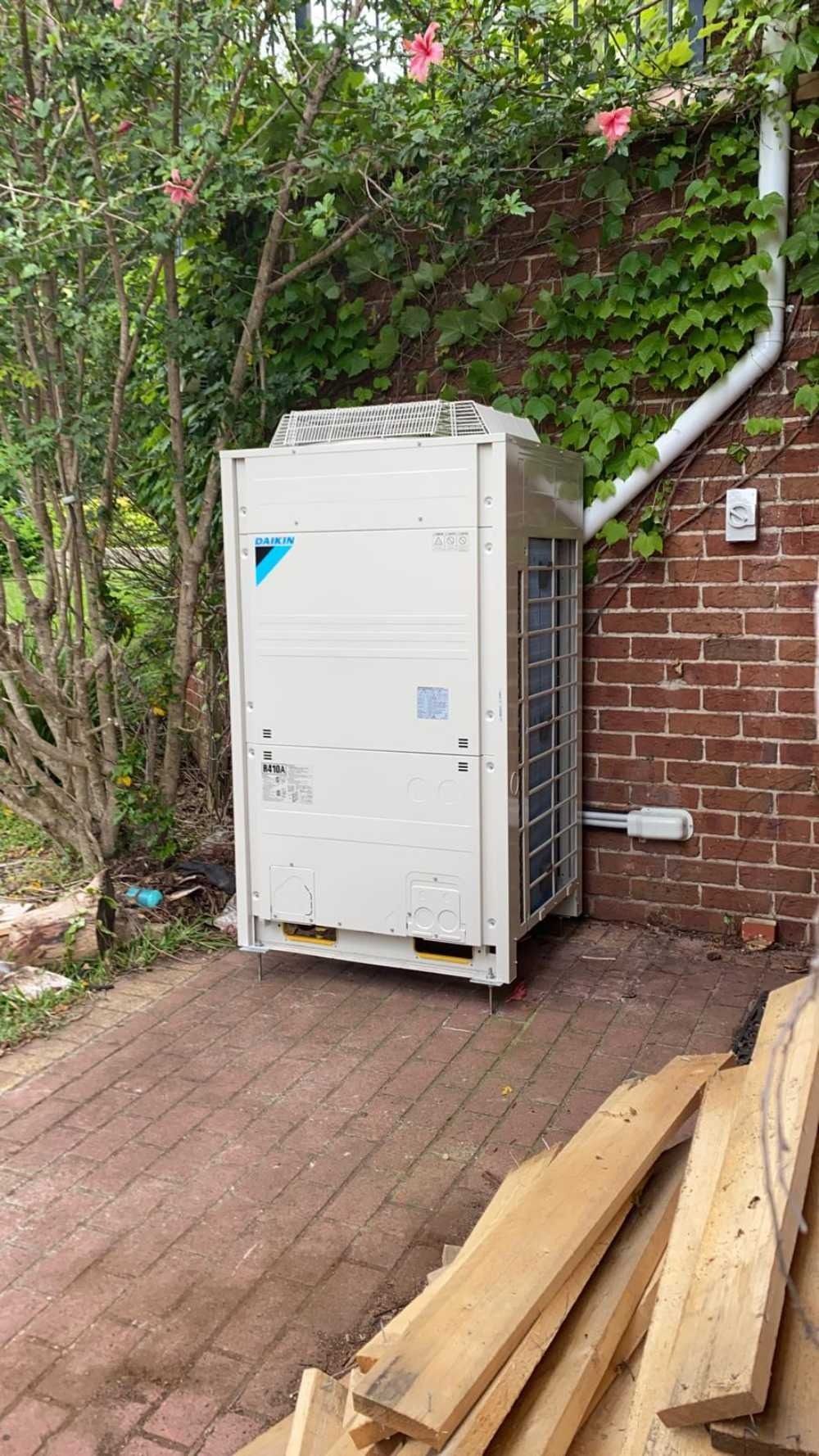 A White Air Conditioner is Sitting Next to a Brick Wall — Cool Heat Air Conditioning in Albion Park, NSW