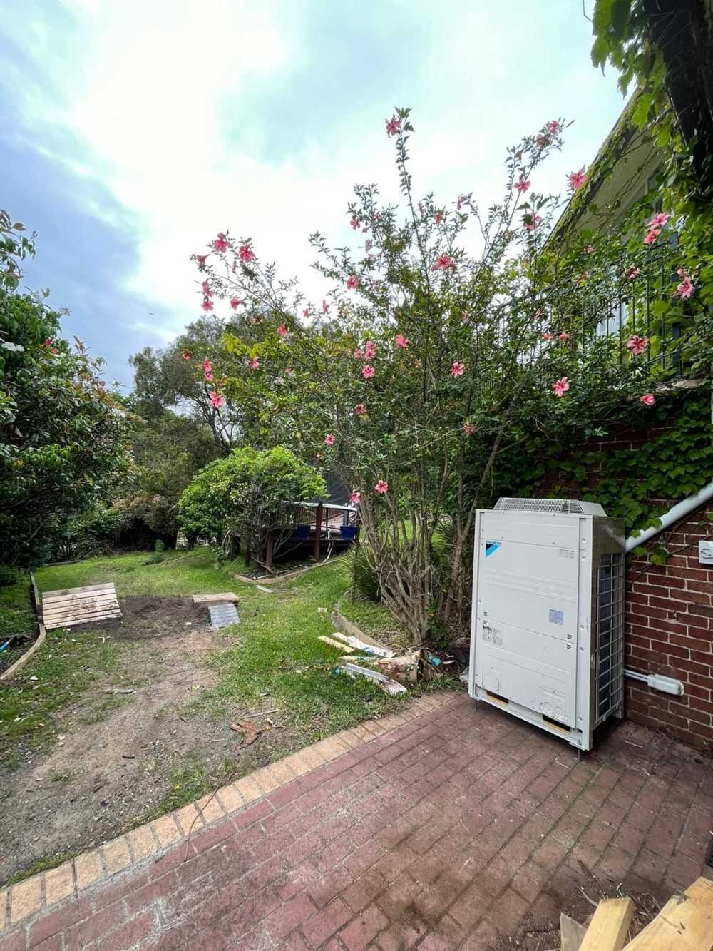 A Large Air Conditioner is Sitting on a Brick Patio in a Backyard — Cool Heat Air Conditioning in Albion Park, NSW