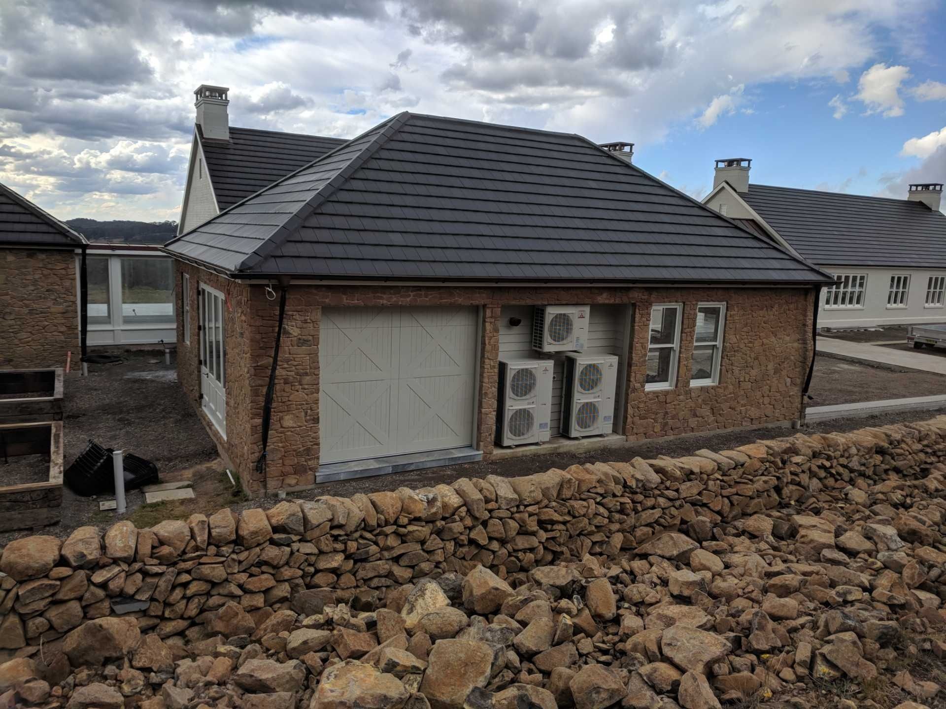 A Brick House With a Black Roof and a Stone Wall — Cool Heat Air Conditioning in Albion Park, NSW