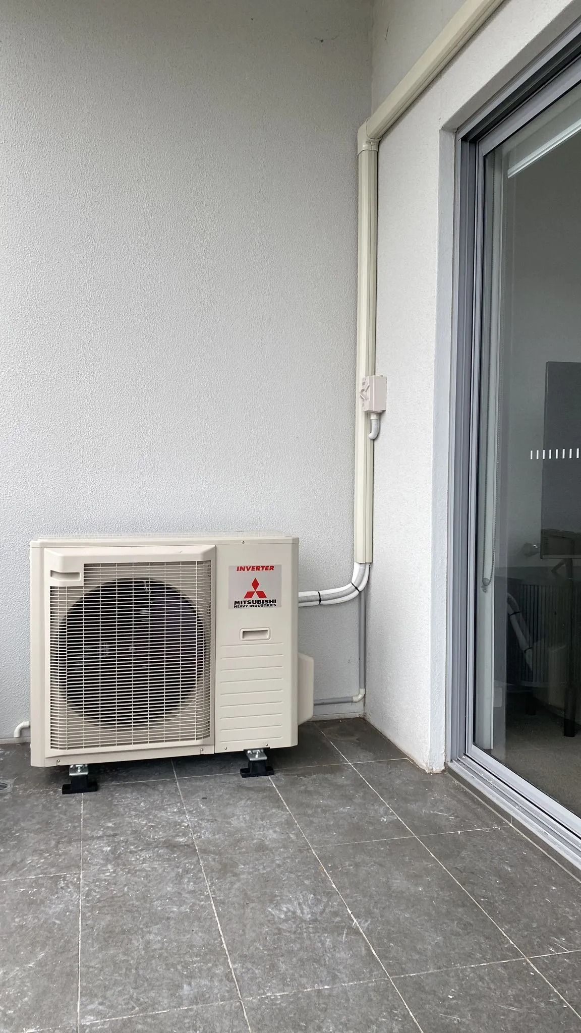 An air conditioning unit is sitting on a tiled balcony — Cool Heat Air Conditioning in Southern Highlands, NSW