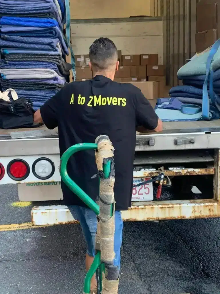 Mover in black shirt loading items from a truck at a moving dock with stacked blue pads.