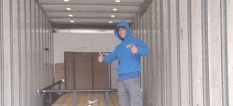 Person in a blue hoodie standing inside a shipping container, giving a thumbs-up.