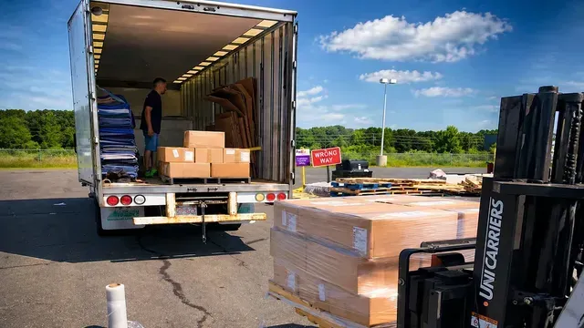 Open truck loading dock with pallets and boxes in a parking lot under a blue sky.