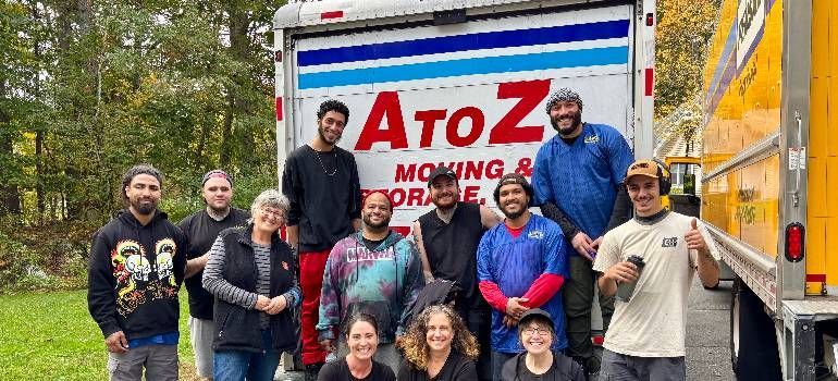 AtoZ Moving crew posing beside a moving truck in a wooded outdoor setting.