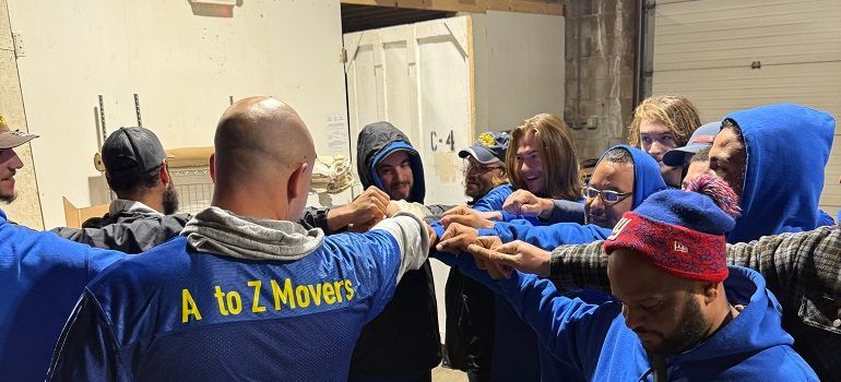 Blue-uniformed movers stand in a circle with arms extended for a team huddle indoors.