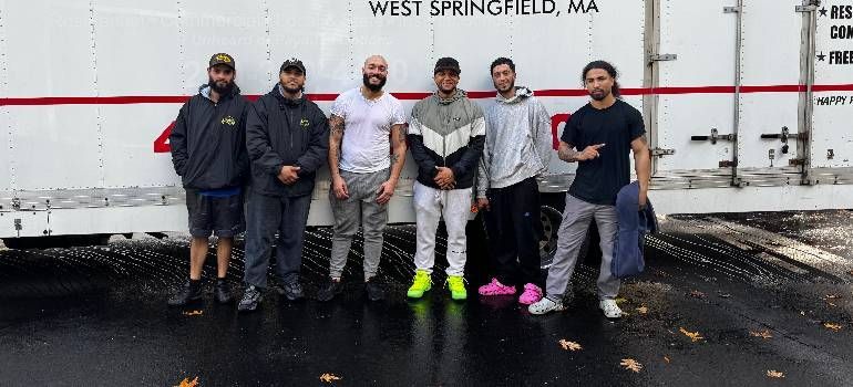 Six people stand in a parking lot before a trailer labeled West Springfield, MA.