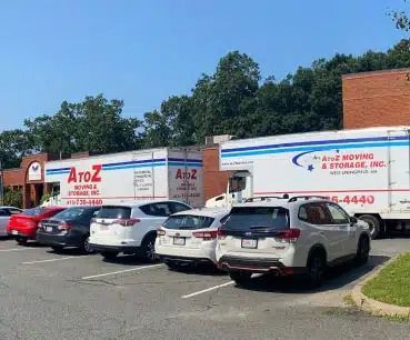 Parked white A to Z Moving and Storage trucks and cars outside a warehouse on a sunny day
