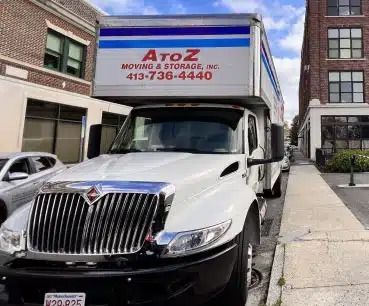 White moving truck parked on a city street between buildings, with A to Z Moving & Storage sign visible on top.