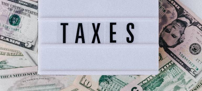 “TAXES” on a white sign surrounded by U.S. dollar bills.