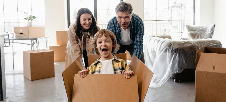 Family smiling in a bright living room, with a child sitting in a cardboard box during a move