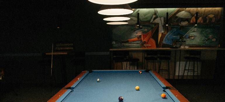 Pool table in a dimly lit room with a few scattered billiard balls and overhead lights