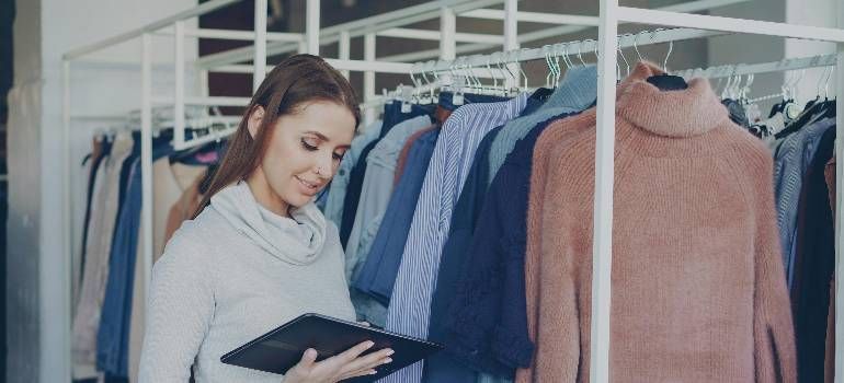 Woman browsing clothes on a rack in a boutique, holding a tablet