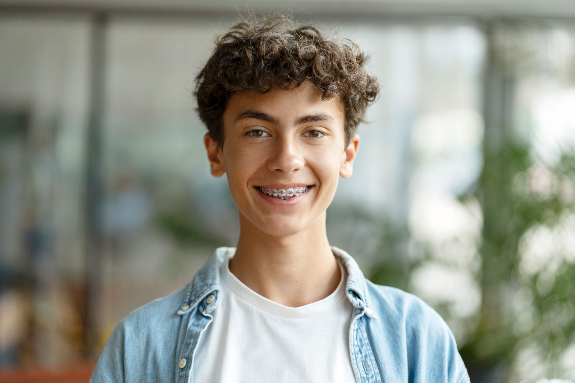 Young person standing indoors wearing a denim shirt over a white tee.