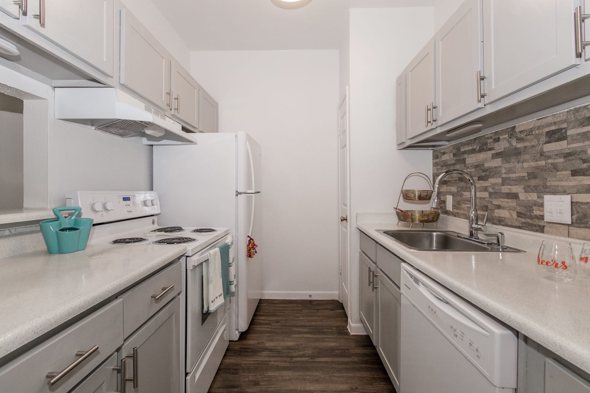 Galley kitchen with white appliances, gray cabinets, white countertops, and wood-look flooring.